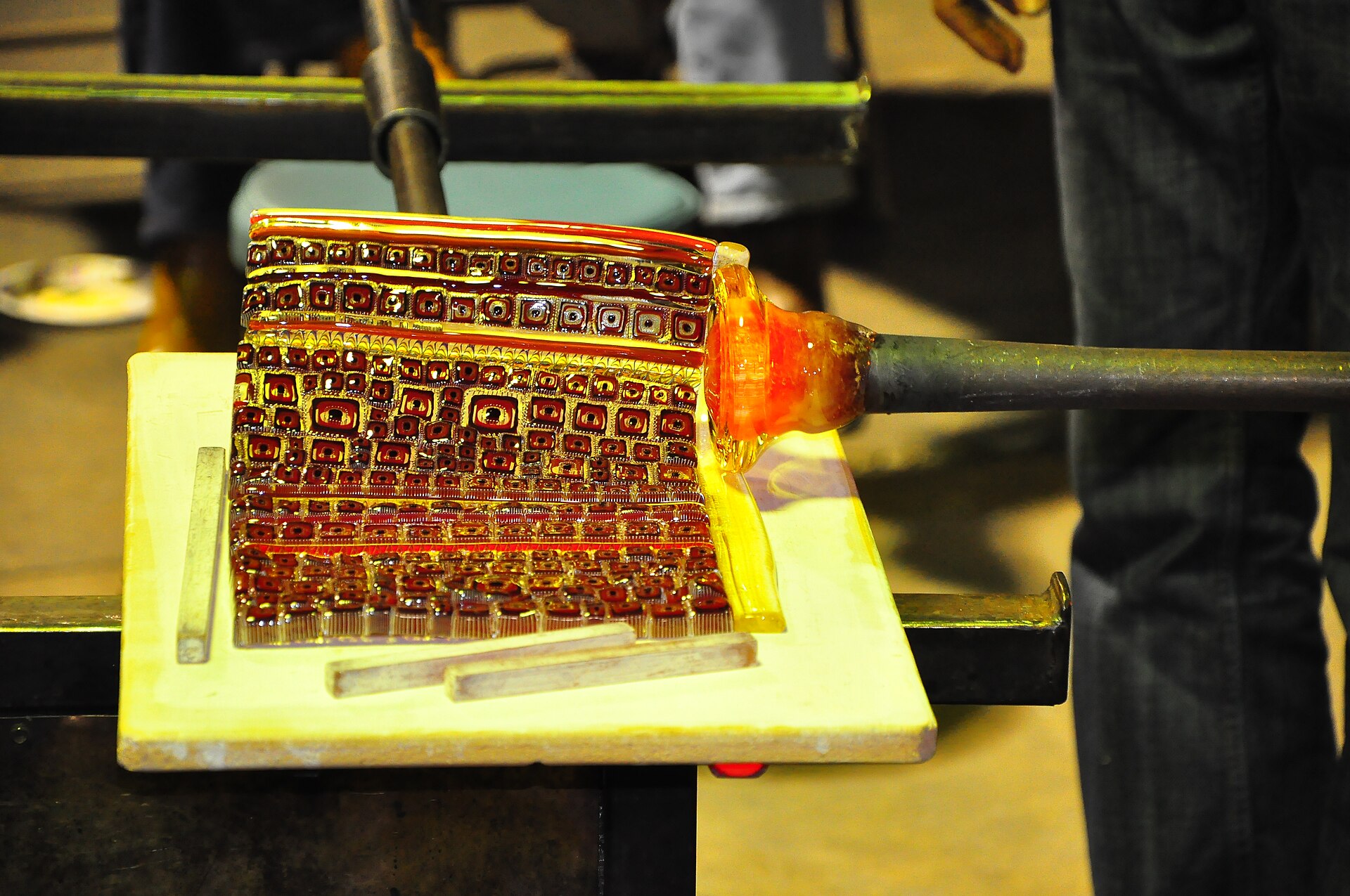 A hot glass form rolling across rows of colorful murrine tiles