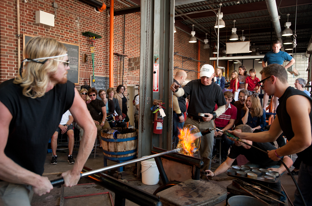 A glassblowing team shaping a hot piece in a working studio