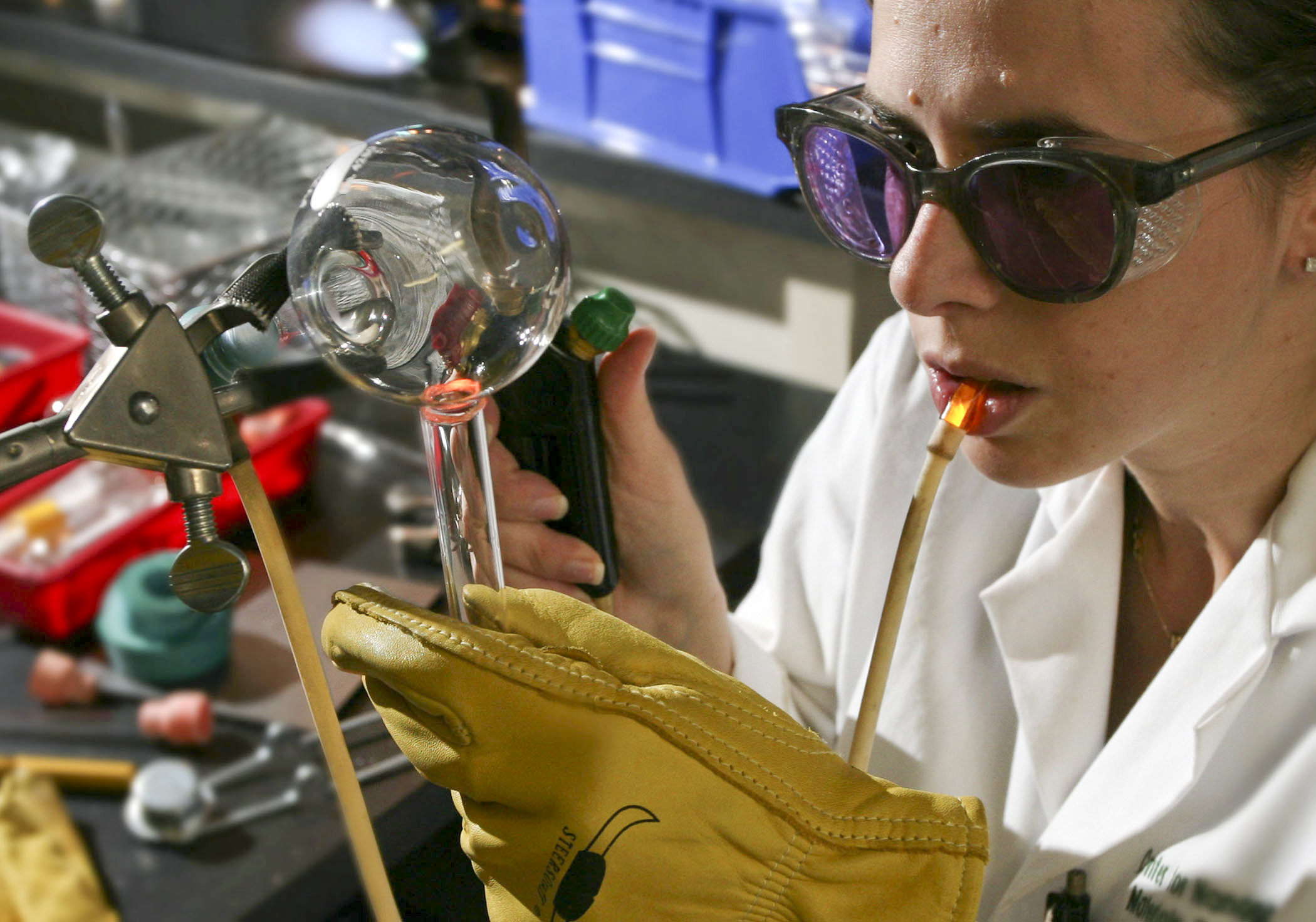 A glassworker finishing a clear vessel while blowing through a pipe